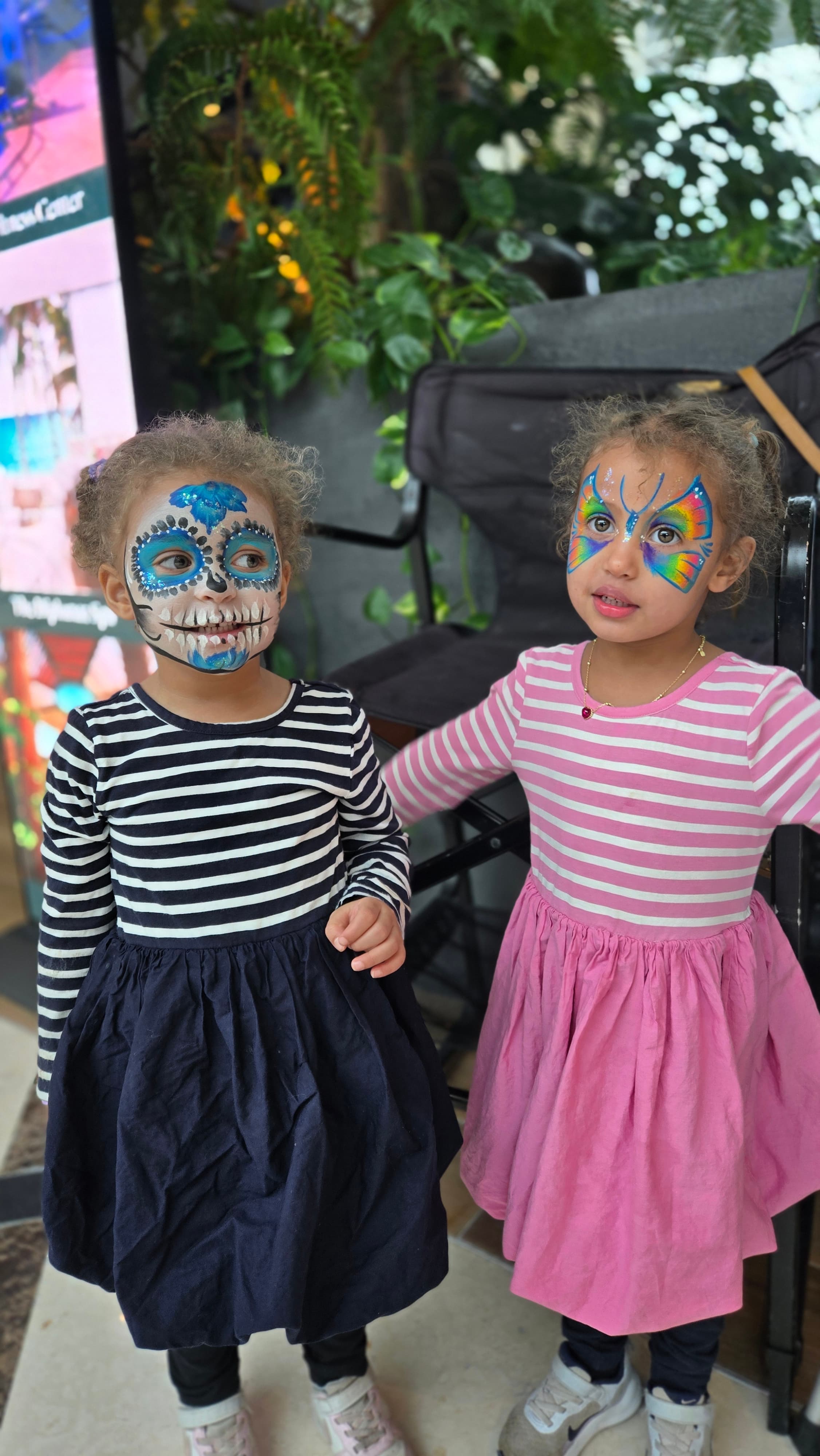 Two young girls with colorful butterfly and sugar skull face paint wearing striped dresses.