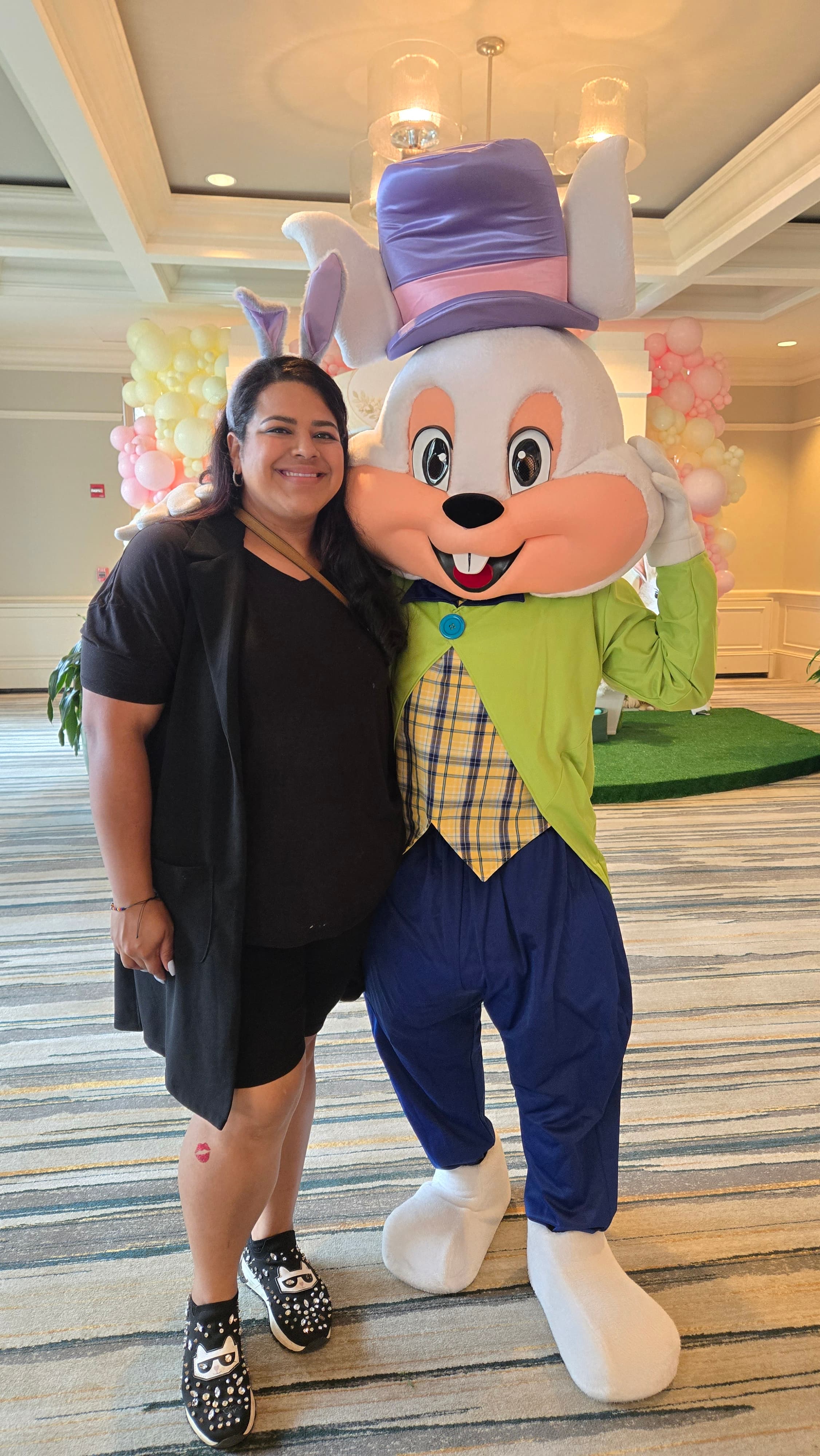 Smiling woman in black poses with a large rabbit mascot wearing a purple top hat.