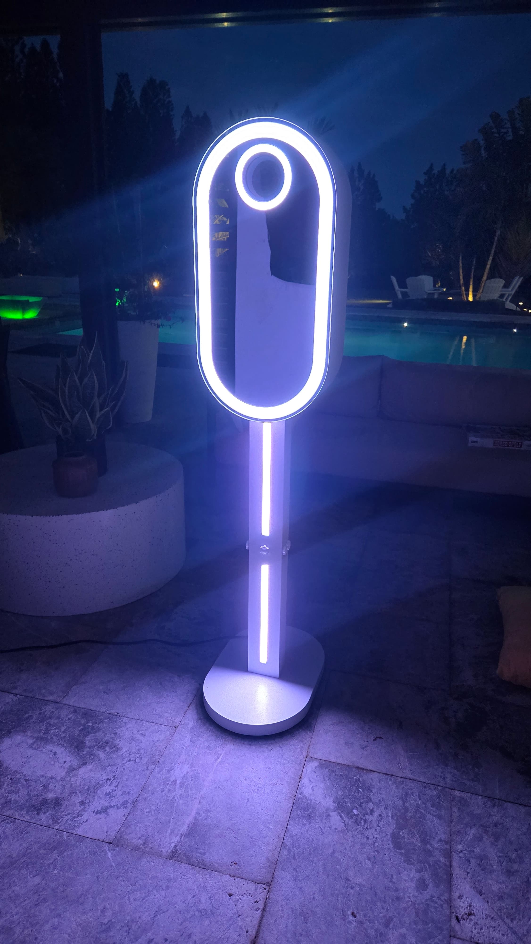 Sleek white photo booth with glowing oval lights on a stone patio at night.