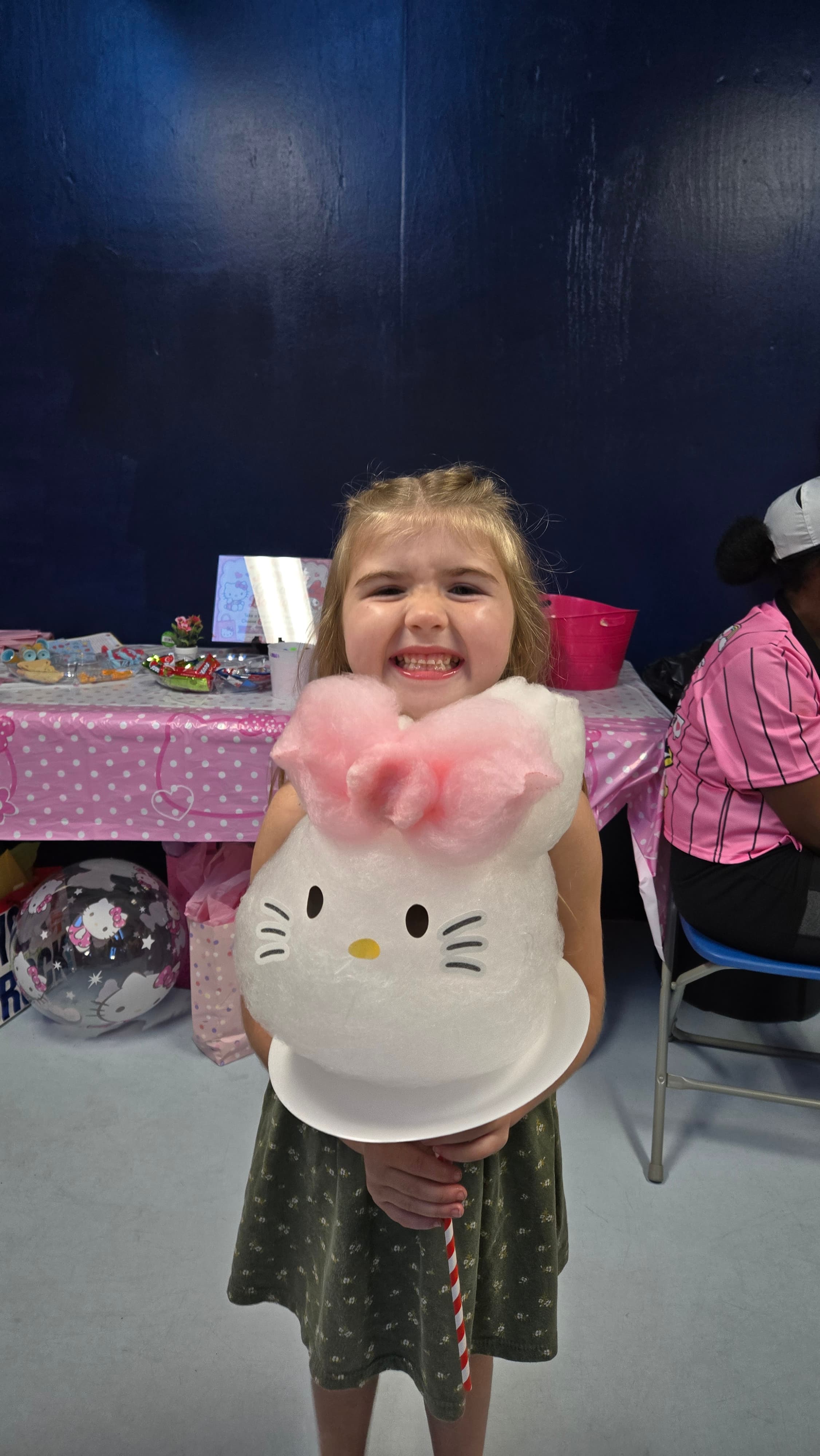 Smiling young girl holding a large Hello Kitty cotton candy with a pink bow.