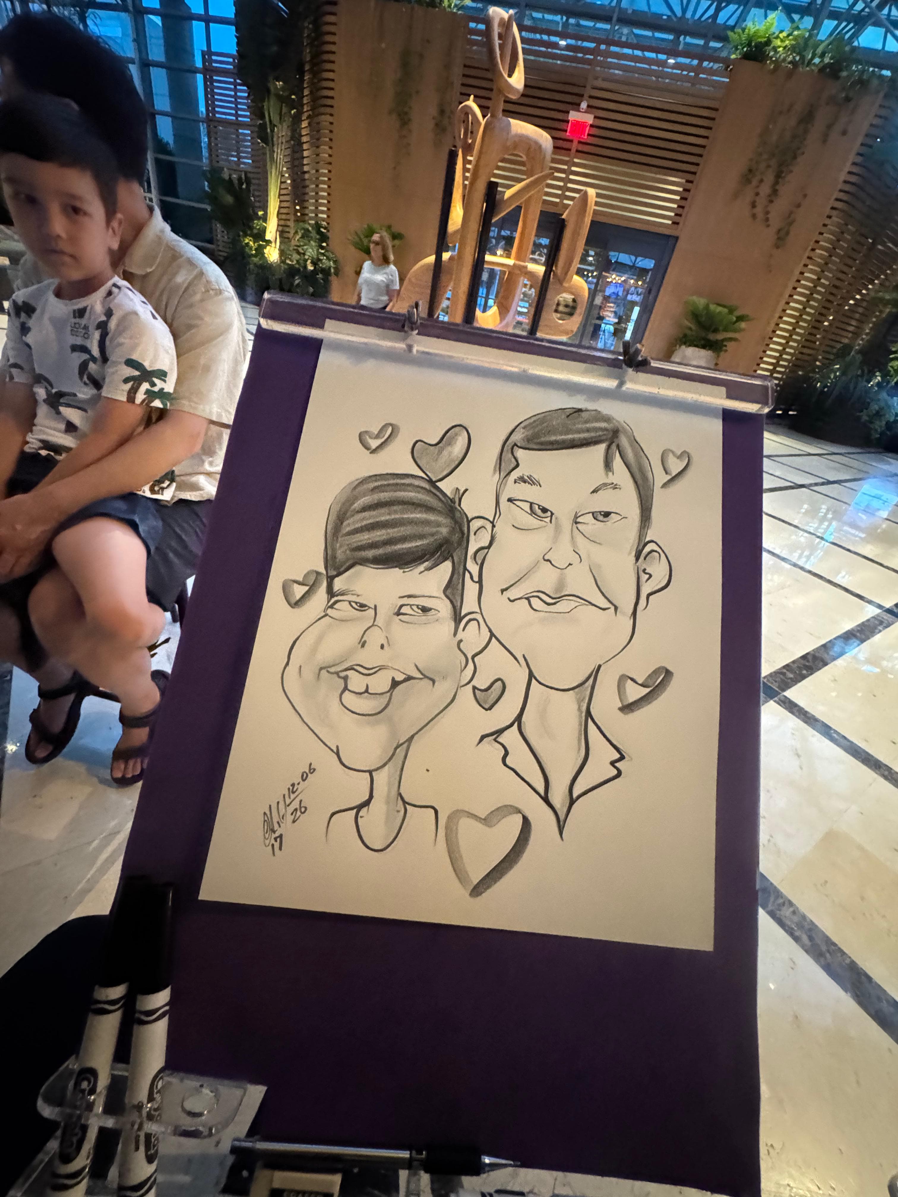Black and white caricature of a man and boy on an easel with floating hearts.
